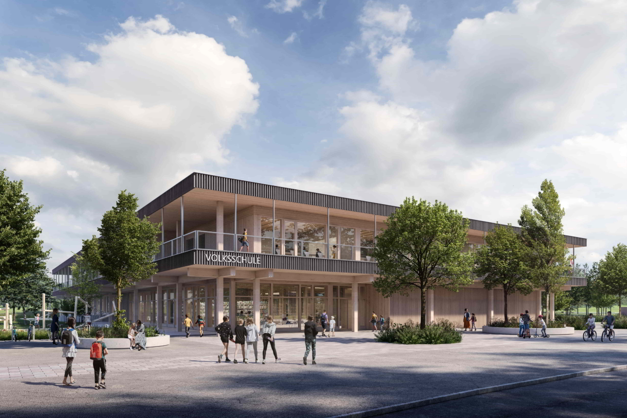 Foto der Volksschule von Grambac - Flachdachbau mit Bäumen rund um das Gebäude und im Vordergrund ein betonierter Platz